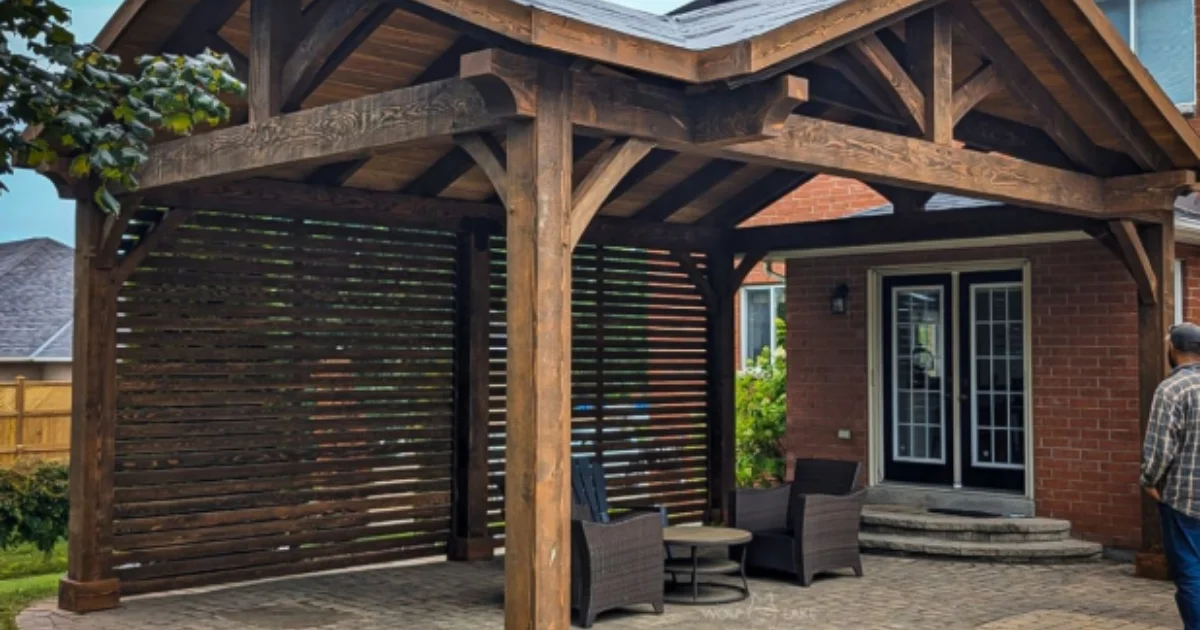 Timber pavilion with dark wood beams and slatted privacy wall, located in a backyard patio.